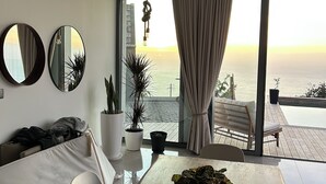 Un soggiorno moderno con un grande tavolo di legno, due specchi tondi e vista sul mare attraverso ampie finestre.