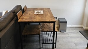 A dining area with a wooden table, benches, a clock, and decorative shelves. - Beach house in pembrokeshire with sea views (Freshwater East)