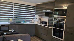 A modern kitchen with a built-in oven, microwave, and a large window with blinds. - Beach house in pembrokeshire with sea views (Freshwater East)
