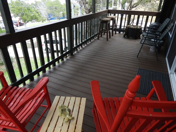 A covered deck with red chairs, a small table, and a grill area.