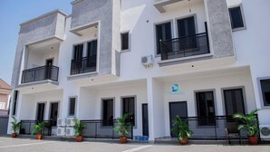A modern multi-story building with balconies, air conditioning units, and potted plants. - DEOSEA APARTMENTS (Abuja)