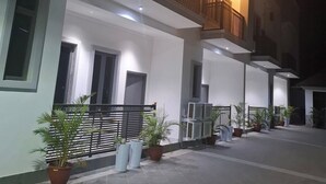 A modern two-story building with a balcony on the upper floor, potted plants, and a tiled courtyard. - DEOSEA APARTMENTS (Abuja)