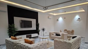 A modern living room with tufted sofas, a flat-screen TV, and a marble floor. - DEOSEA APARTMENTS (Abuja)