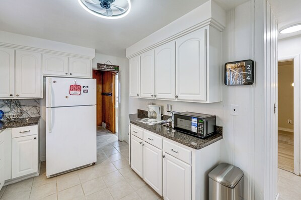 A kitchen with white cabinets, a refrigerator, a microwave, and a trash can.