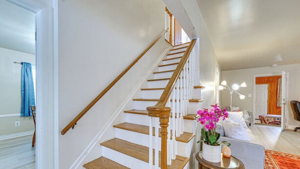 Una escalera con escalones de madera y barandillas blancas que conduce a un dormitorio con cama, mesita de noche y un jarrón de flores.