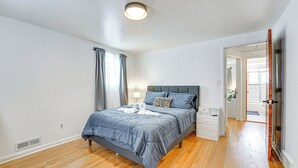Un dormitorio con cama, mesitas de noche, una lámpara y una puerta que da a otra habitación.