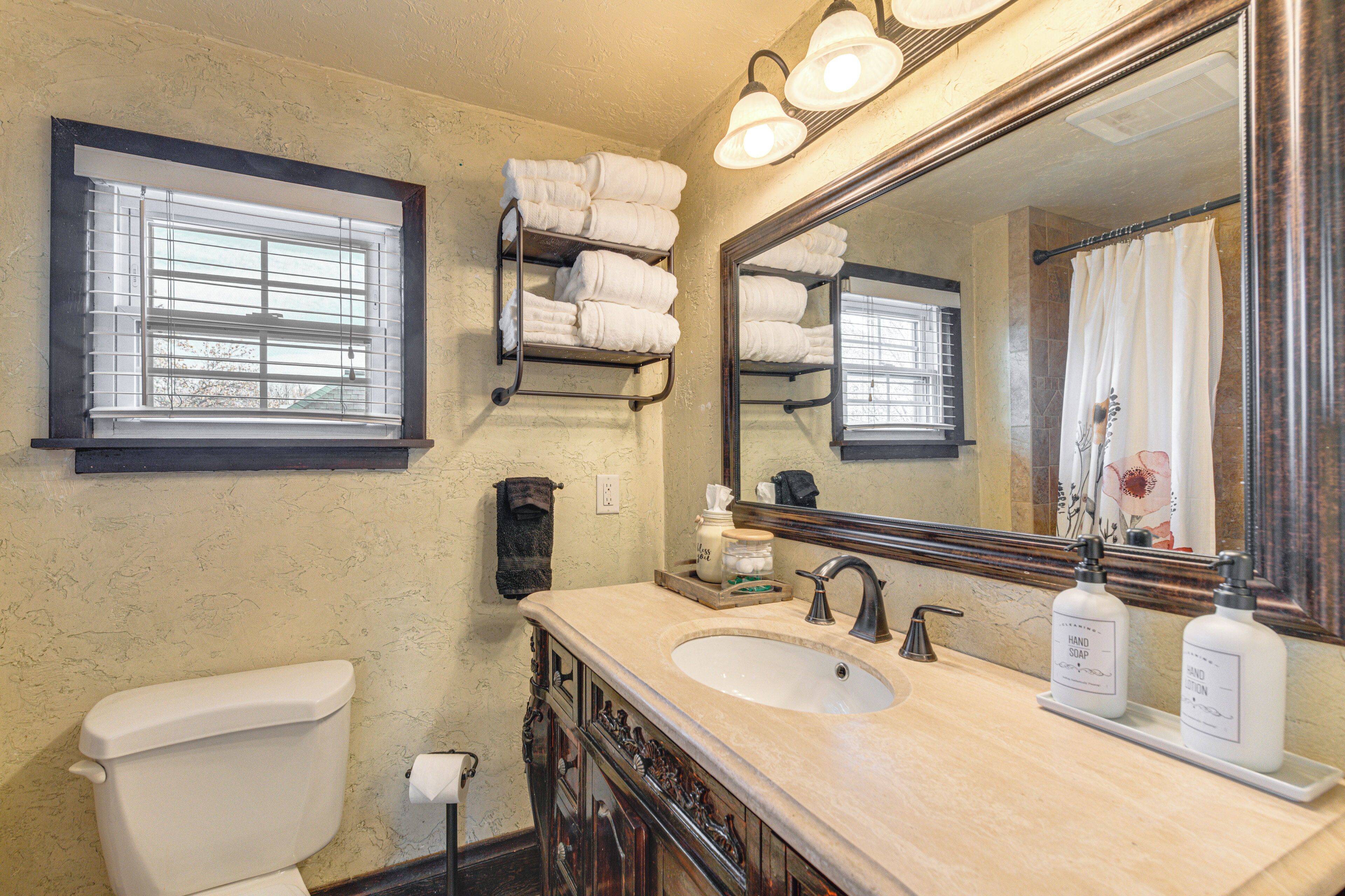 A bathroom with a toilet, sink, and mirror. There are towels hanging on a rack and a shower curtain.