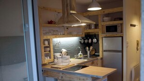 A kitchen with wooden cabinets, a microwave, a refrigerator, and a sink. There are stools and a window with a view of the outside.