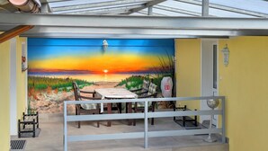 Een eetgedeelte met uitzicht op een zonsondergangsmural, een tafel, stoelen en een balustrade.