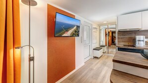 Een moderne hotelkamer met een houten vloer, een flatscreen televisie aan de muur, een ingebouwde koffieapparaat en uitzicht op het strand door het raam.