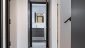A modern hallway with a view into a bathroom featuring a toilet, sink, and mirror.