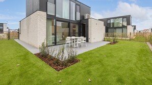 A modern two-story house with large windows, a well-maintained lawn, and outdoor seating.