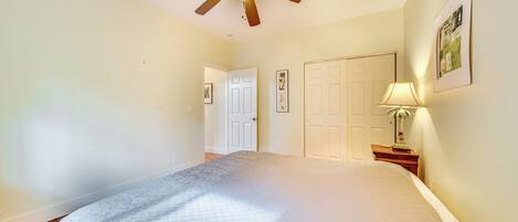 A bedroom with a bed, a ceiling fan, a nightstand with a lamp, and a door leading to another room.