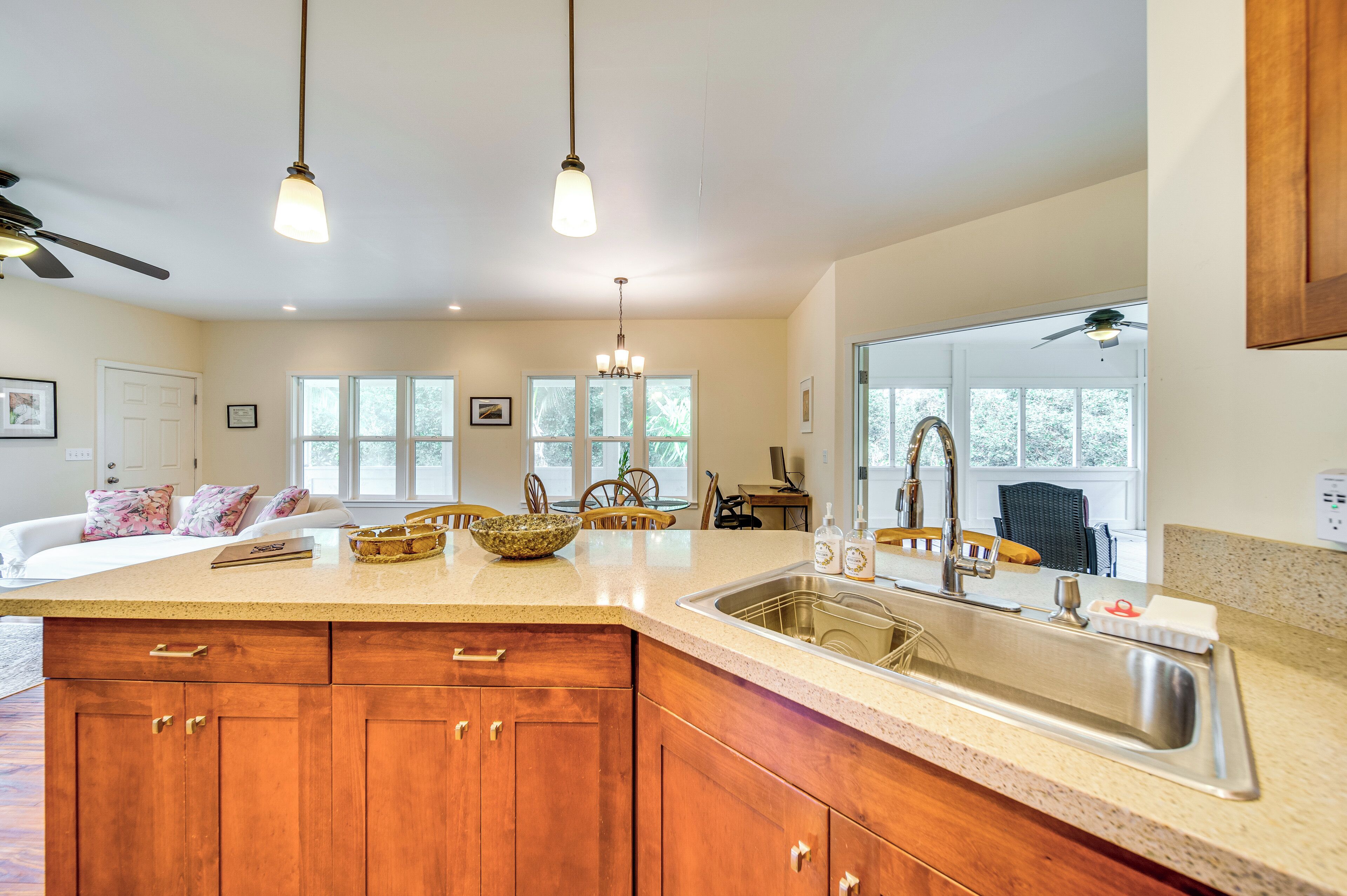A kitchen with a large island, wooden cabinets, a stainless steel sink, and pendant lighting.
