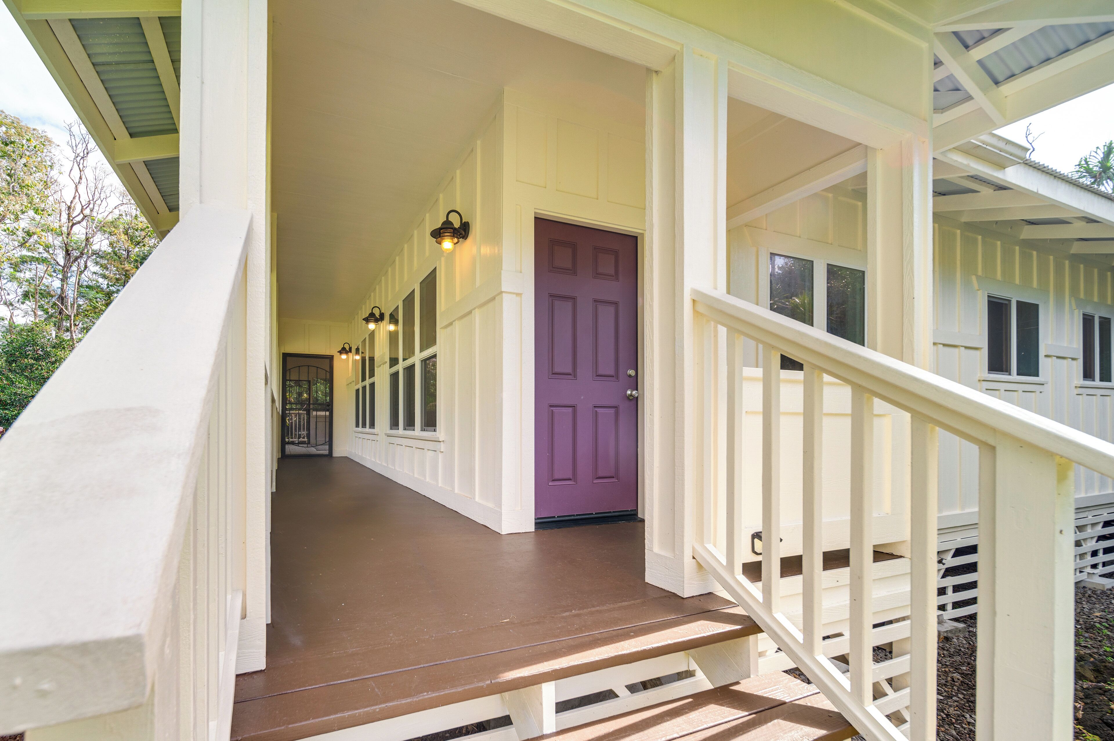 A covered porch with a purple door, white railings, and a wooden staircase leading to the entrance.