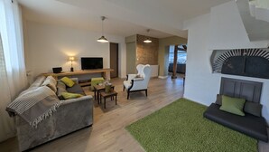 Een moderne woonkamer met een bank, een fauteuil, een televisie en een open haard.