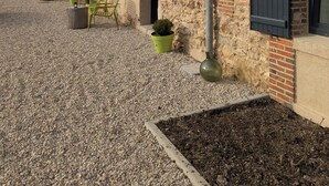 Een gebouw van natuursteen met een binnenplaats van grind, met buiten zitplaatsen en plantenpotten.