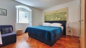 Ein Schlafzimmer mit einem Bett, einem Nachttisch, einer Lampe, einem Sessel und einem Fenster.