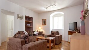Ein Wohnzimmer mit einer Sofagarnitur, einem Couchtisch, einem Fernseher und einem Bücherregal.