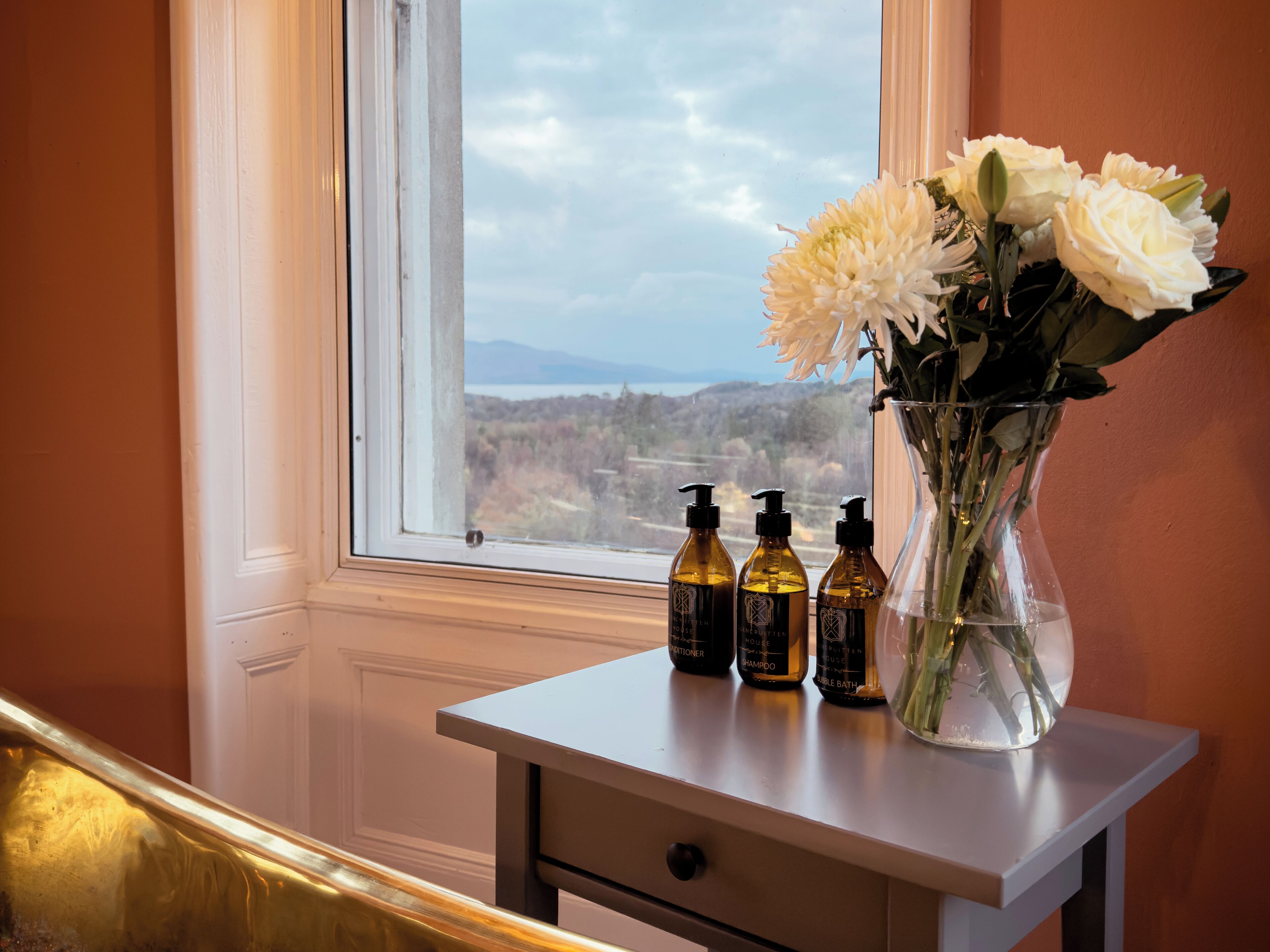 A bathroom vanity with a vase of white flowers and three bottles of hair care products.