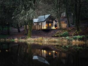 A rustic cabin with a stone exterior, a wooden deck, and a pond in the foreground. - Glencruitten House (Oban)