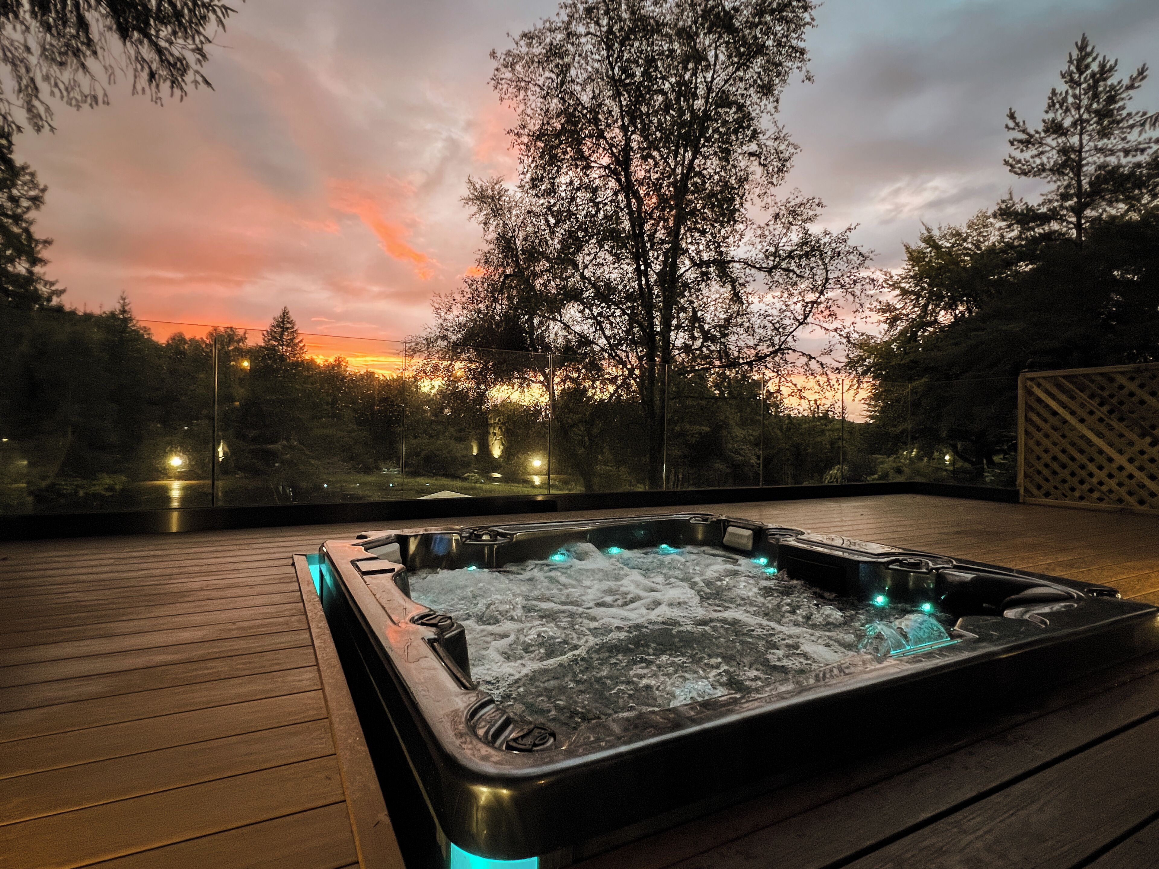A hot tub on a wooden deck with a sunset view.