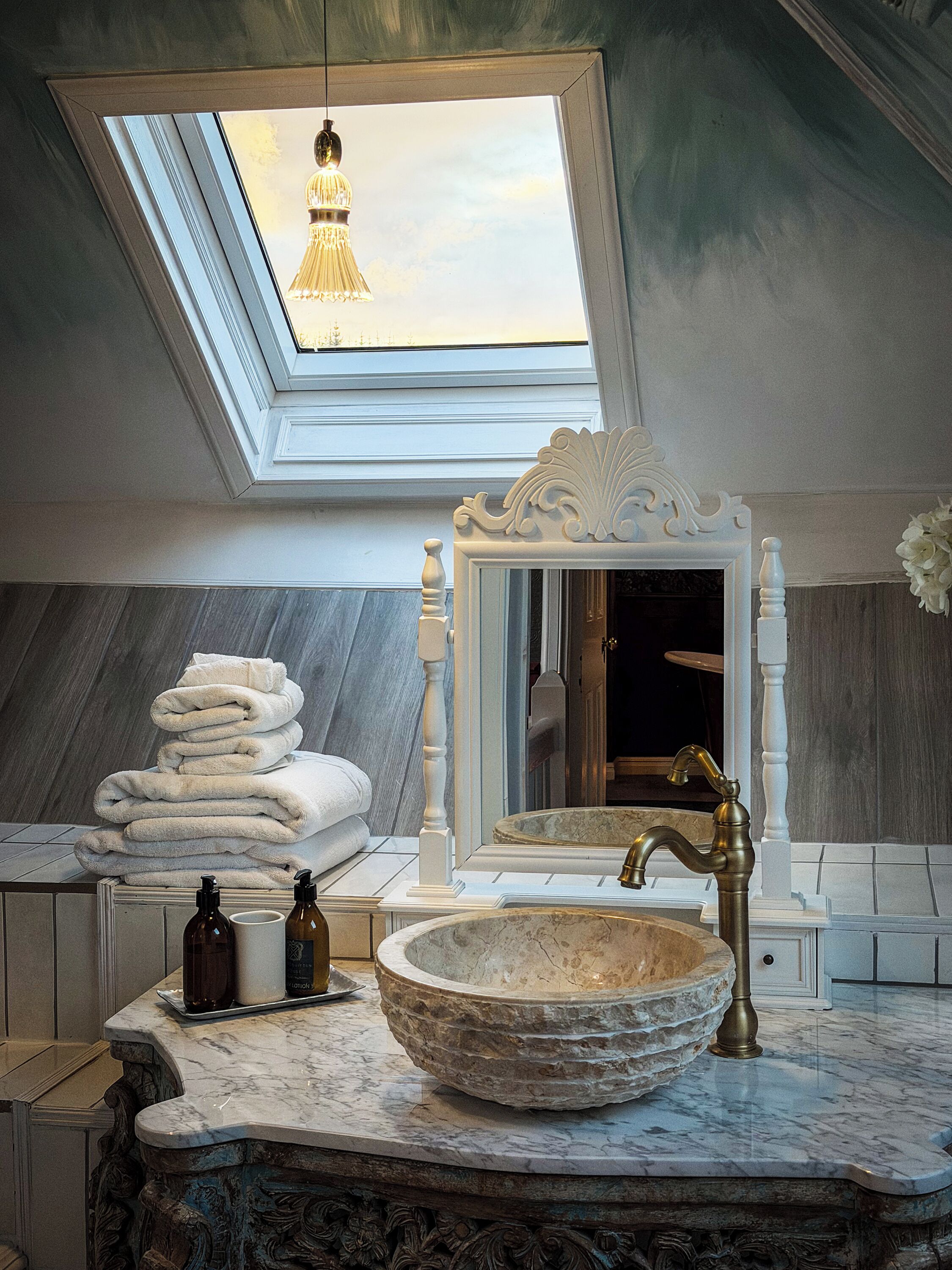 Une salle de bain dotée d’un puits de lumière, d’un grand miroir, d’un lavabo en marbre et d’une pile d’serviettes.