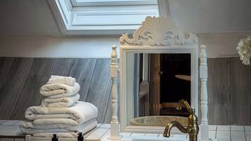 Une salle de bain dotée d’un puits de lumière, d’un grand miroir, d’un lavabo en marbre et d’une pile d’serviettes.