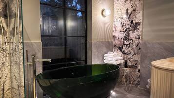 A modern bathroom with a large green bathtub, a glass shower enclosure, and a marble wall with a unique pattern.