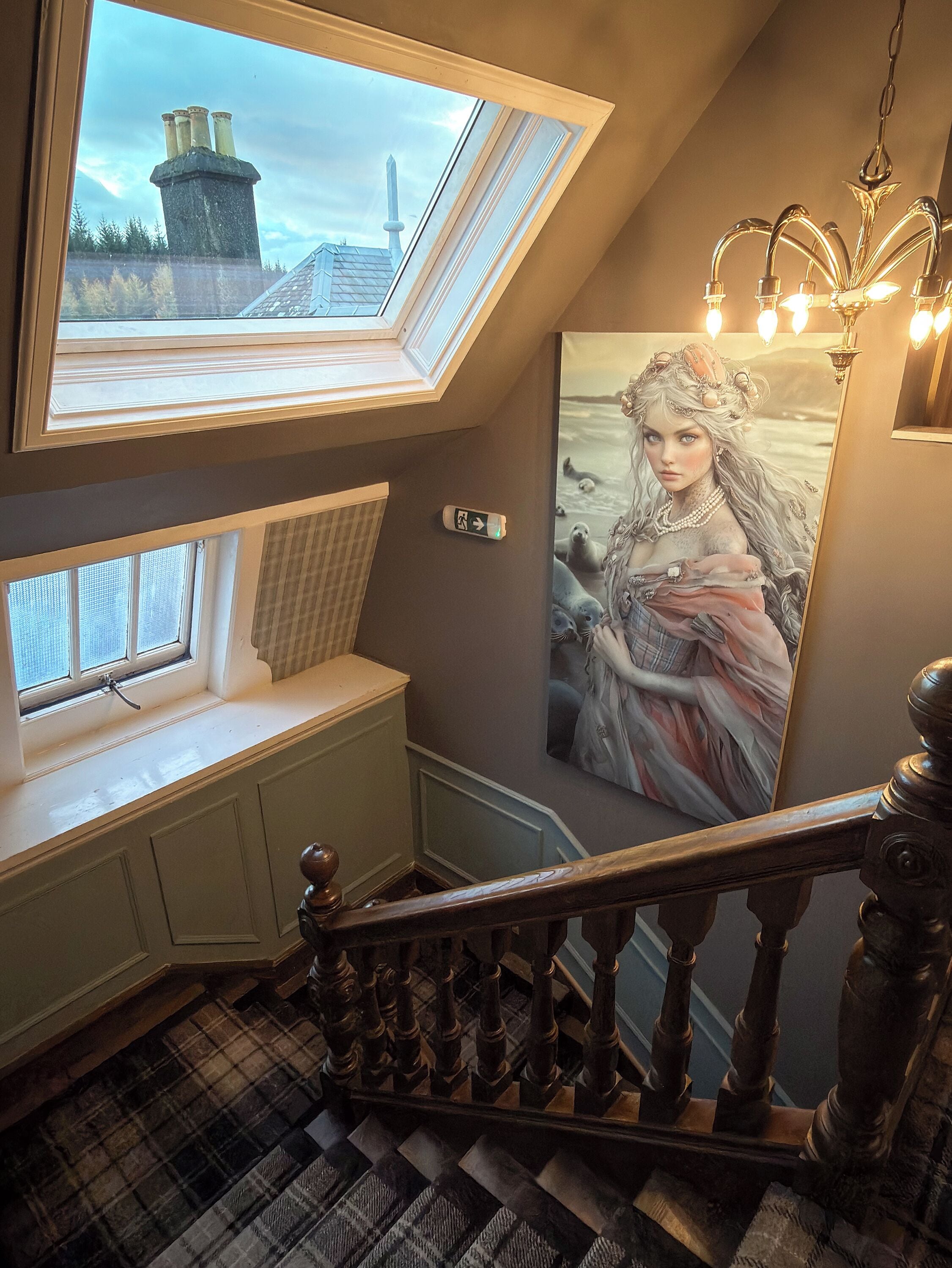 Una escalera con vistas a un paisaje urbano a través de un tragaluz, una obra de arte enmarcada y una barandilla de madera tradicional.