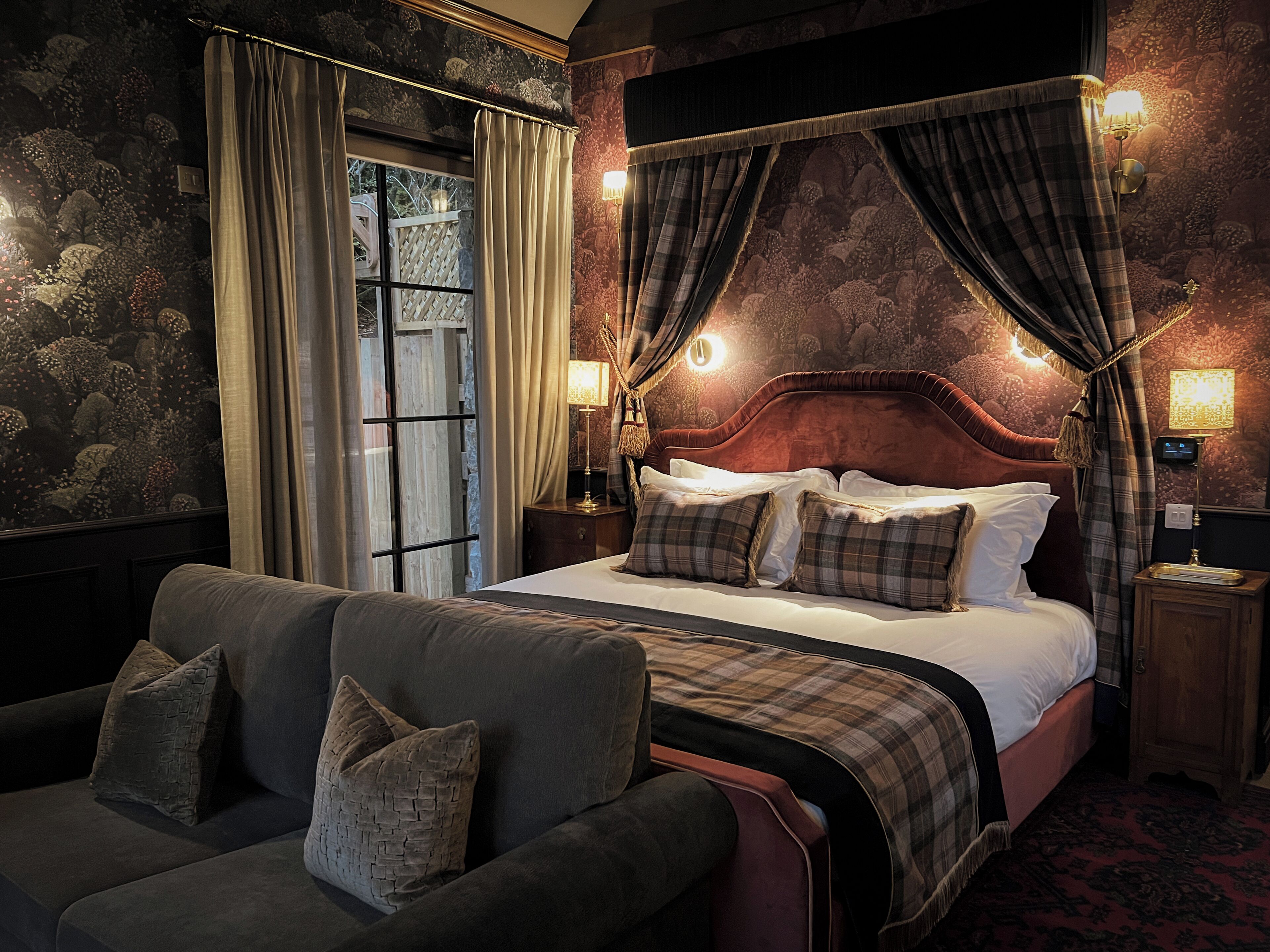 A bedroom with a four-poster bed, a sofa, and a nightstand with a lamp.