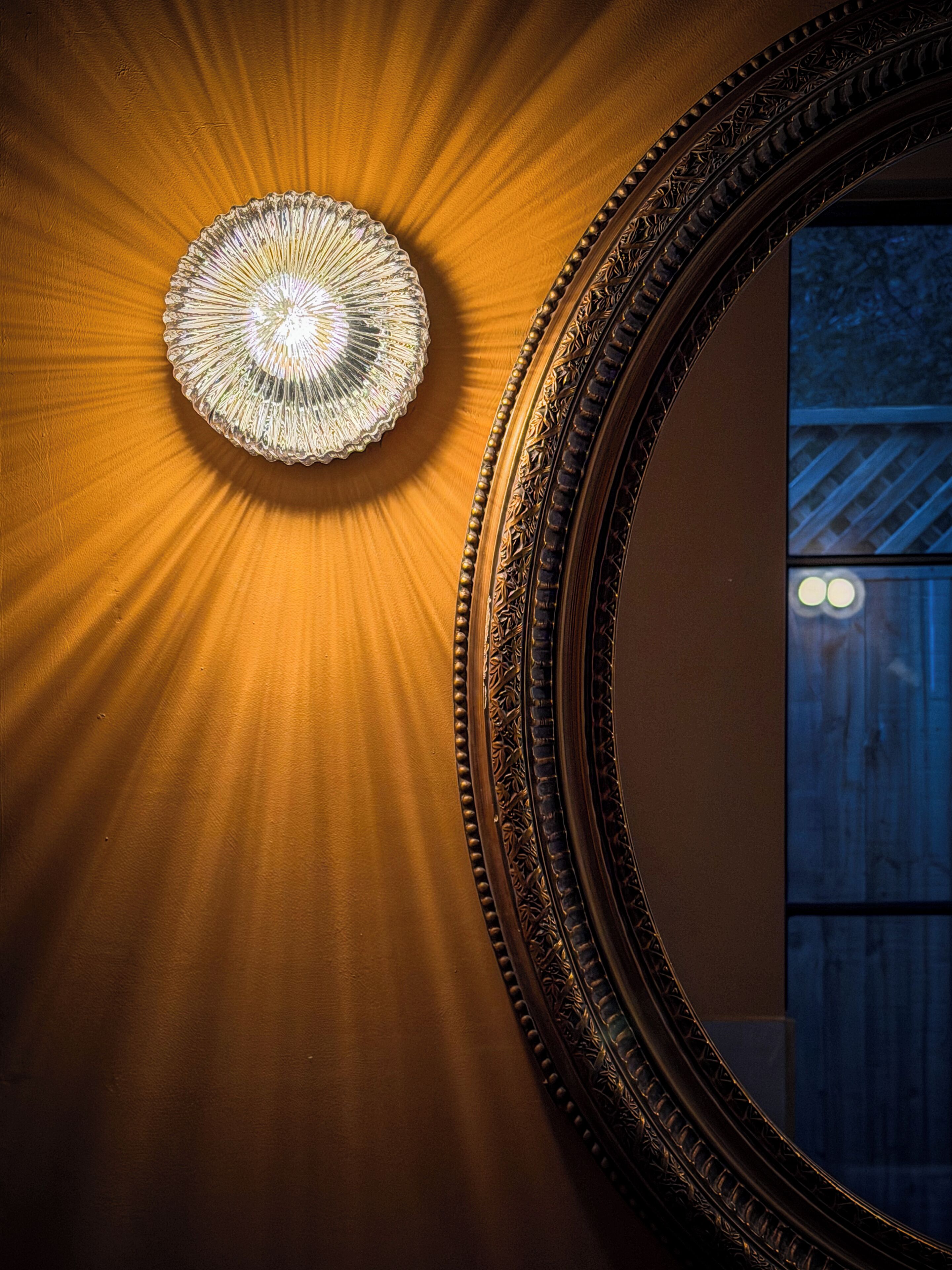 A wall with a decorative light fixture and an ornate mirror.