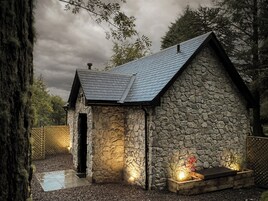 Una casa de piedra con techo inclinado, un porche pequeño y una chimenea.