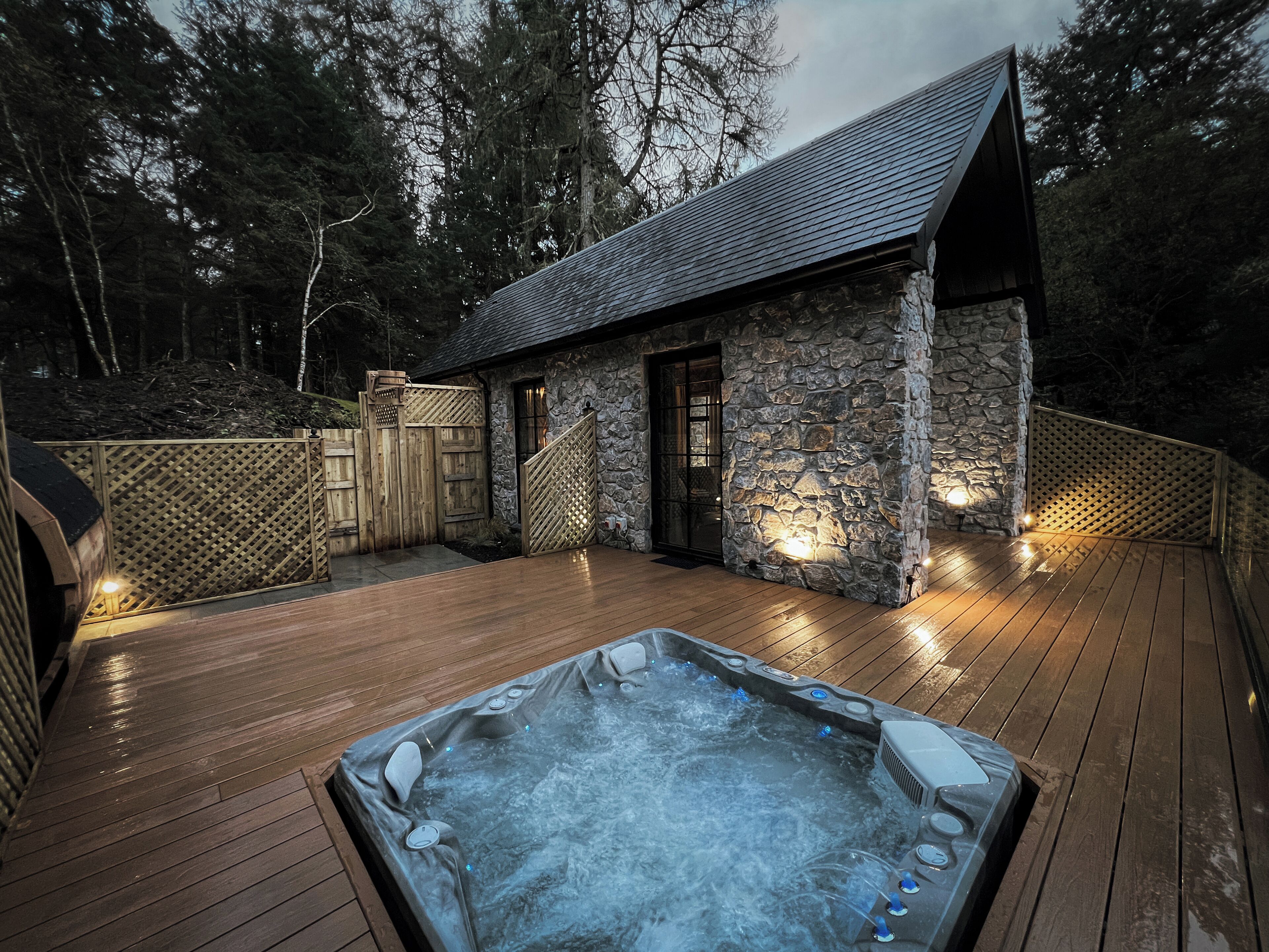 Un jacuzzi en una terraza de madera con un edificio de piedra al fondo.