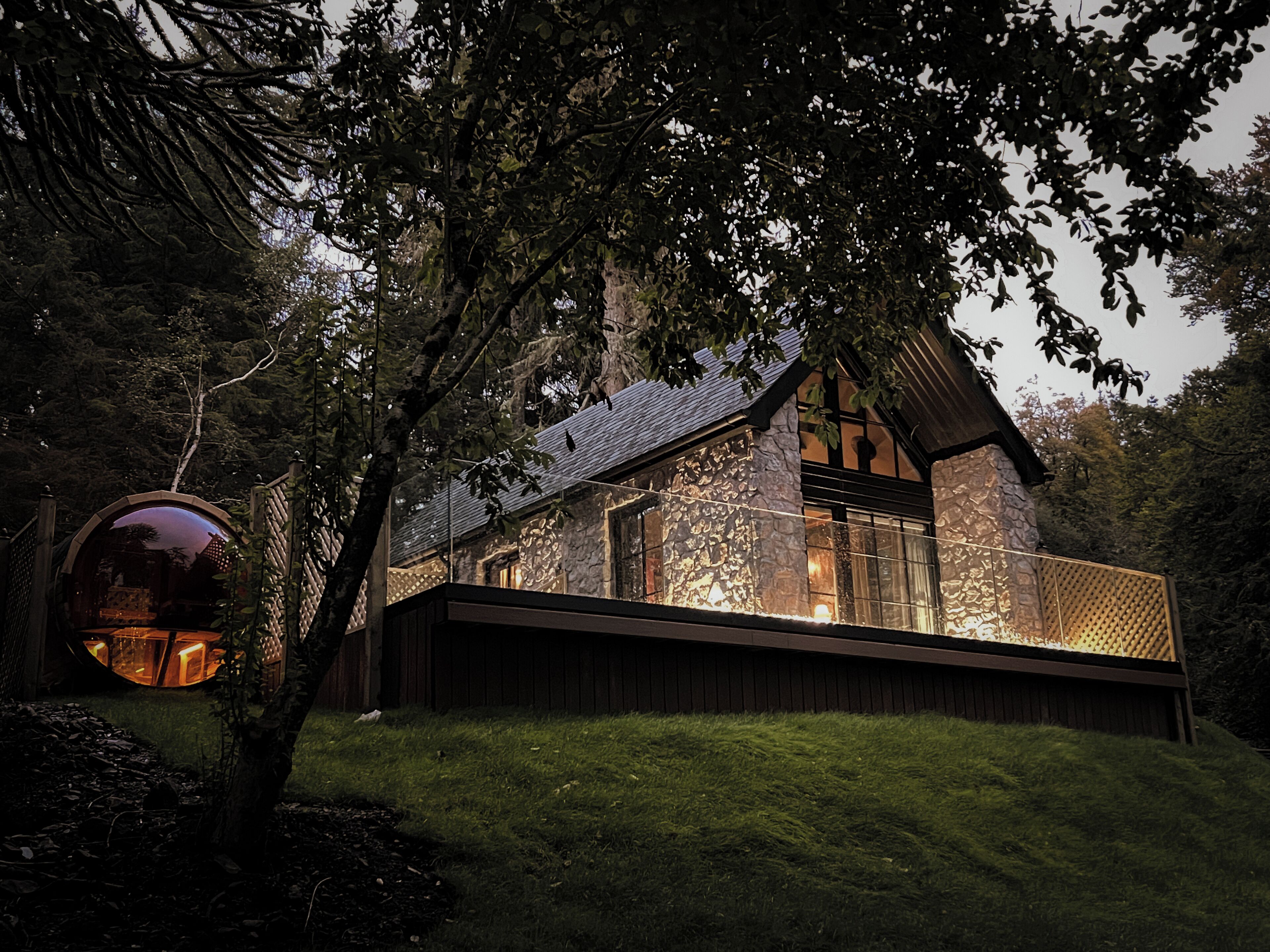 A stone house with a large glass window, surrounded by trees.