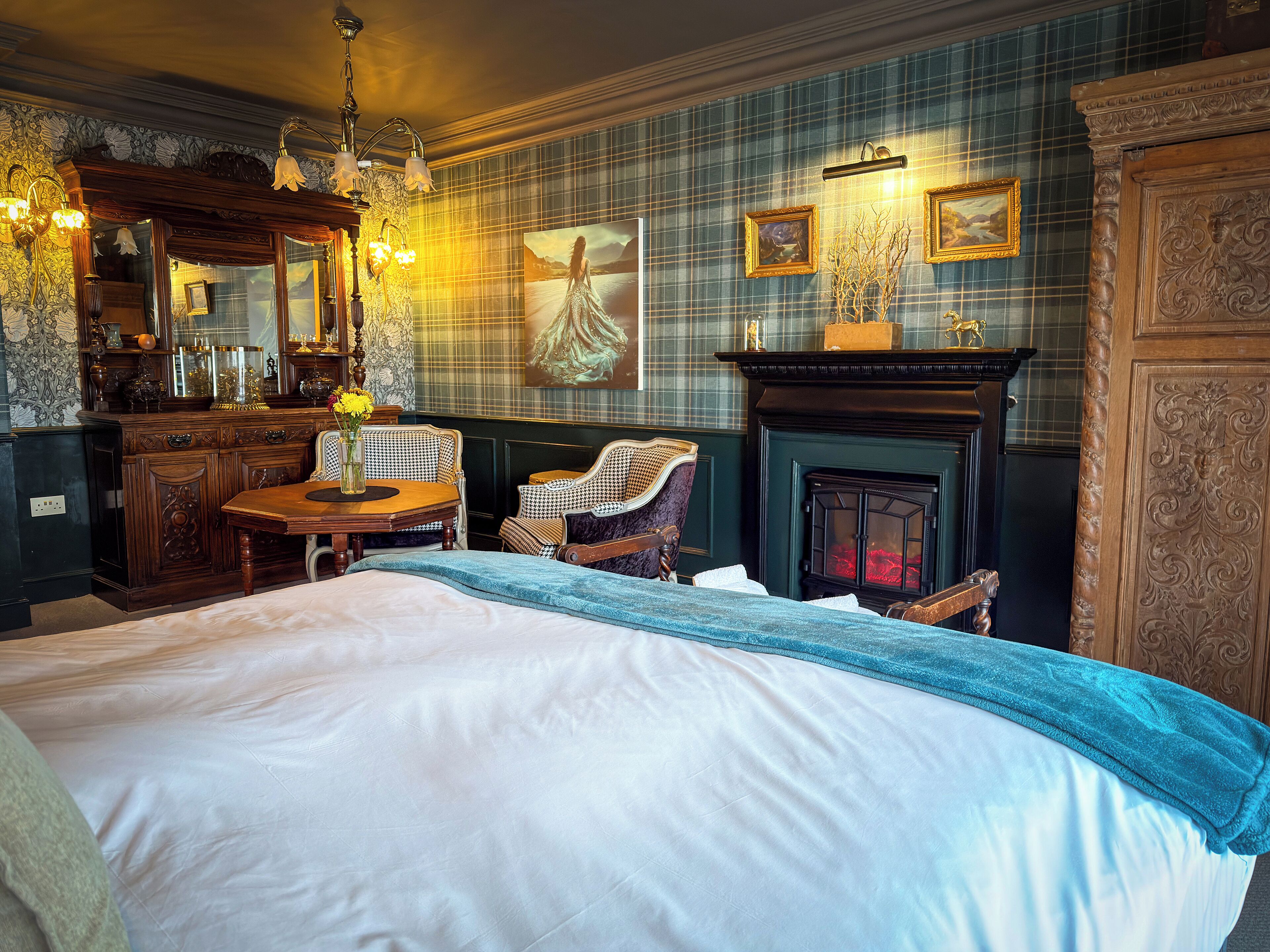 A traditional room with a bed, a fireplace, a dining table, and a mirror.