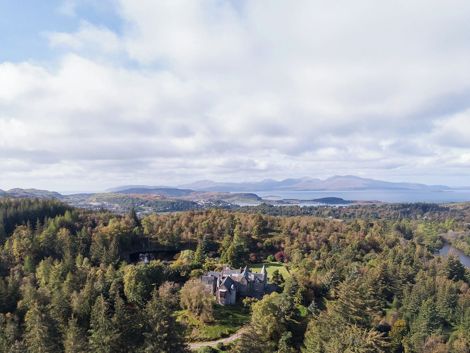 Una extensa propiedad con una casa destacada, rodeada de un bosque denso y un lago al fondo.