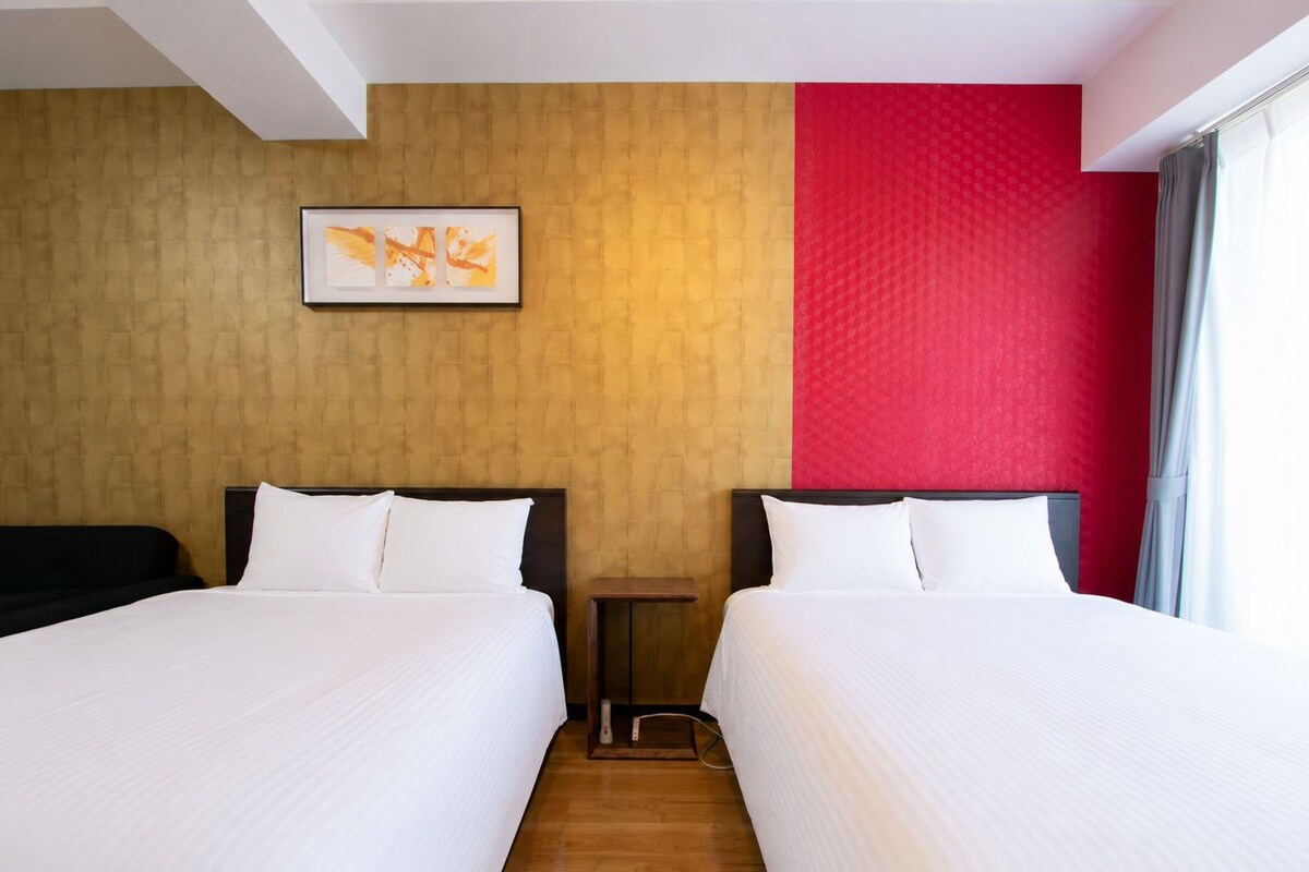 Une chambre d’hôtel avec deux lits, un plancher en bois, un mur d’accent rouge et une œuvre d’art encadrée au-dessus des lits.