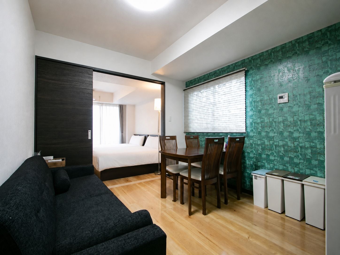 Ein kleines Hotelzimmer mit Bett, einer dunkelgrauen Couch, einem Esstisch mit Stühlen und einer kleinen Küchenzeile.