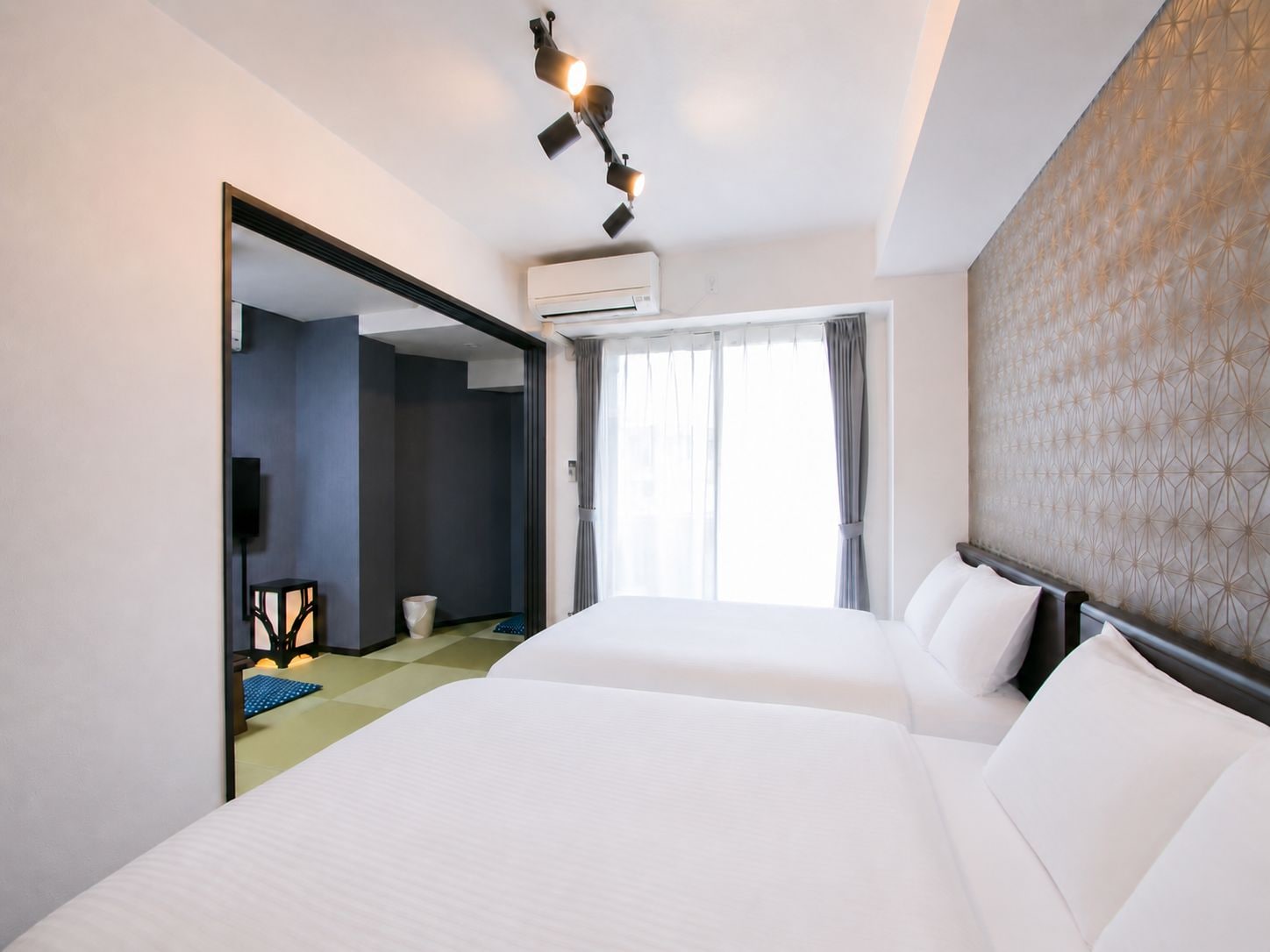 Ein Hotelzimmer mit zwei Betten, einem großen Spiegel, einer Klimaanlage und einem Fenster mit Vorhängen.