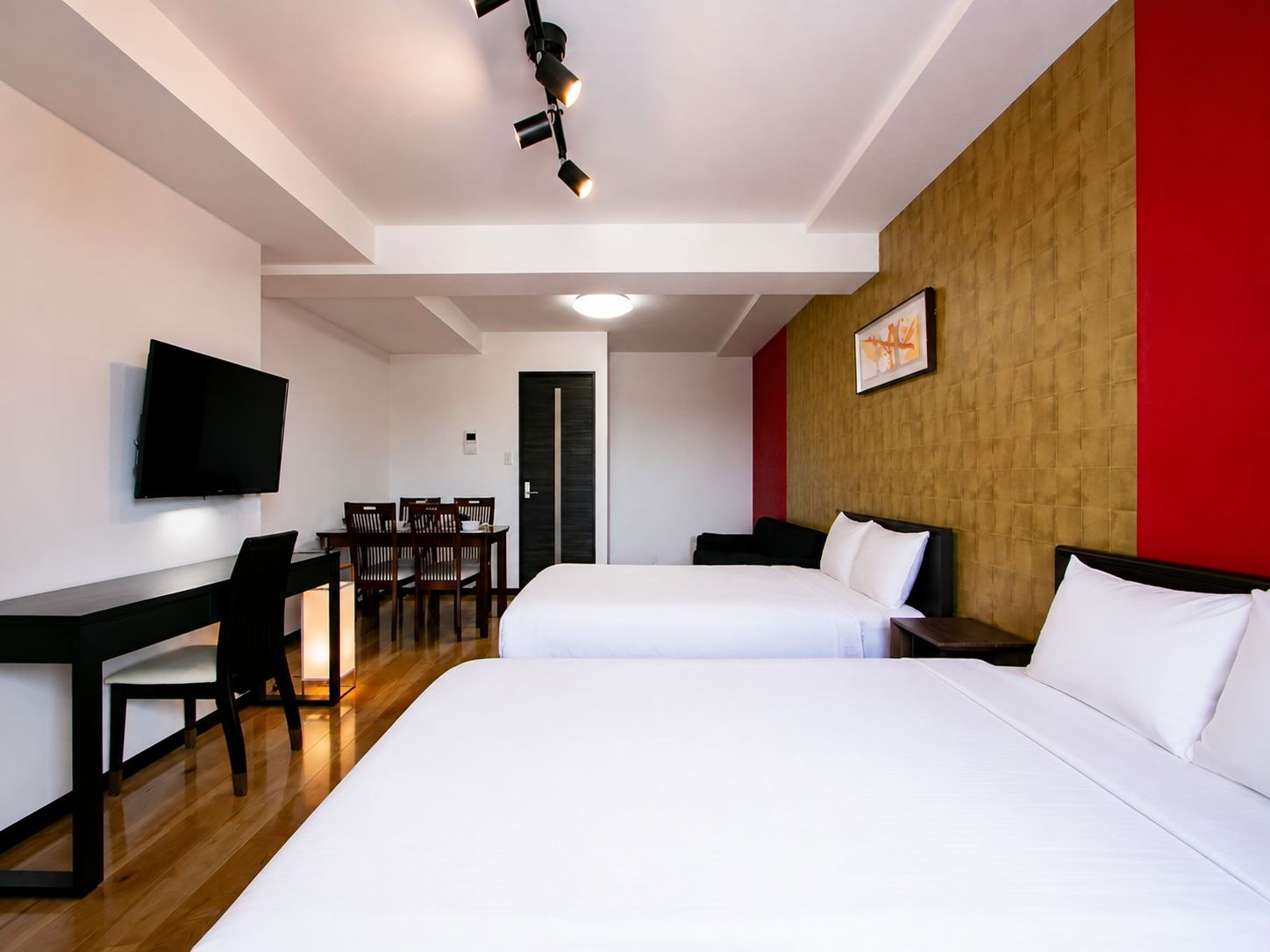 A hotel room with two beds, a desk, a chair, a television, and a door.