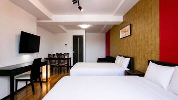 A hotel room with two beds, a desk, a chair, a television, and a door.