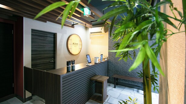 A reception area with a modern design, featuring a wooden reception desk, a round sign with the name 'Minn', and a small seating area. - Randor Residence Tokyo Annex (Tokyo)