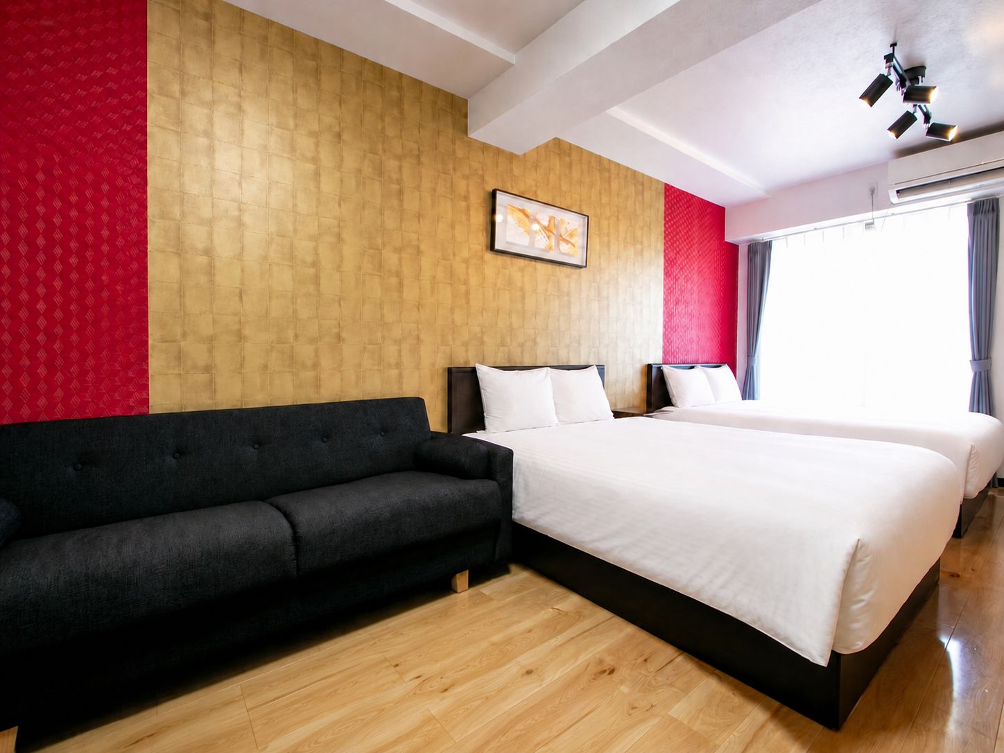 A hotel room with a black sofa, a double bed, and a wooden floor.