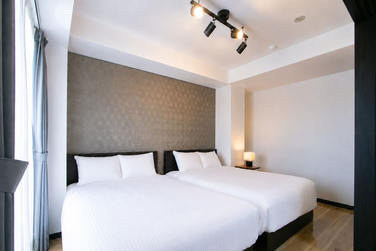 Une chambre d'hôtel avec deux lits, un mur décoré d'un motif, un luminaire au plafond et une table de chevet avec une lampe.