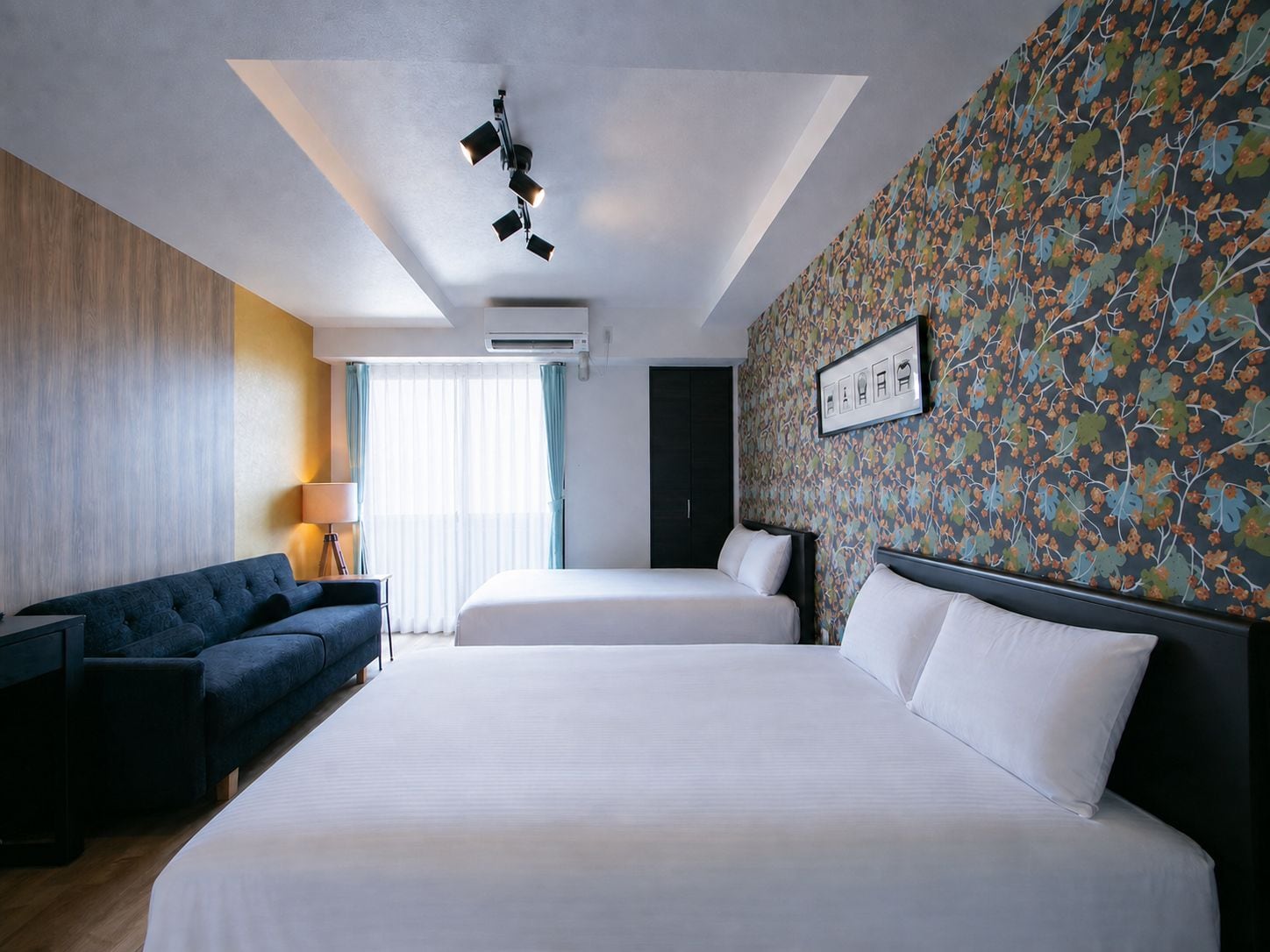 Habitación de hotel con una cama grande, un sofá, un escritorio y un papel tapiz estampado.