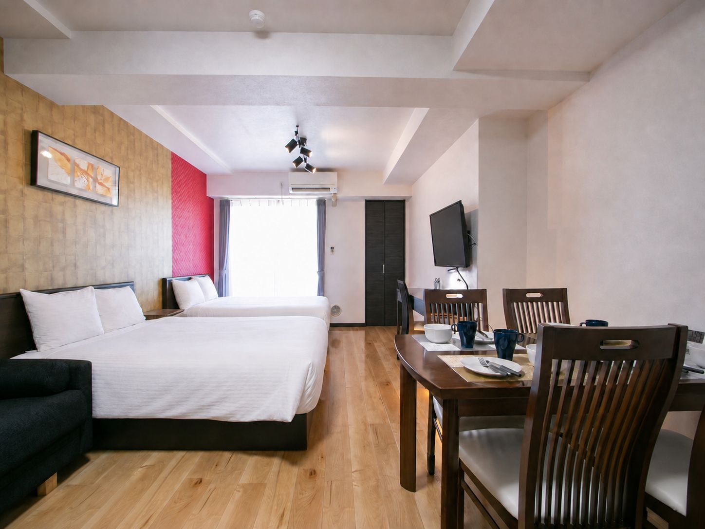 A hotel room with a bed, a desk with chairs, a television, and a window.