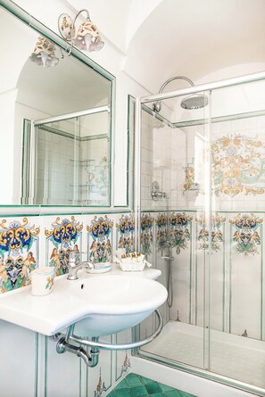 A bathroom with a glass shower enclosure, a white sink with a mirror above it, and decorative tiles on the walls. - 6 Bedrooms, 6 Bathrooms Villa with Private Pool and Sea View, Ravello, Italy (Ravello)