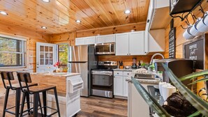 A modern kitchen with wooden ceiling, stainless steel appliances, and a bar area with stools.