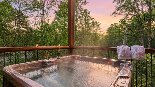 A hot tub on a wooden deck with a view of trees and a sunset.